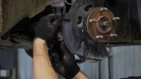 An auto mechanic replacing brake pads on a car wheel at a service station. Stock Footage 297838824