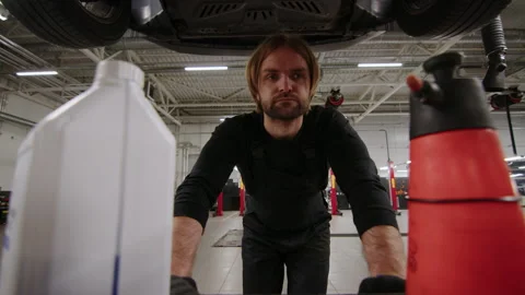 An auto mechanic rolls a cart with tools under the car that will be repaired Stock Footage 240074591
