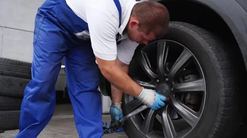 Auto mechanic secures car wheel with torque wrench for precision. Worker in Stock Footage 261026151