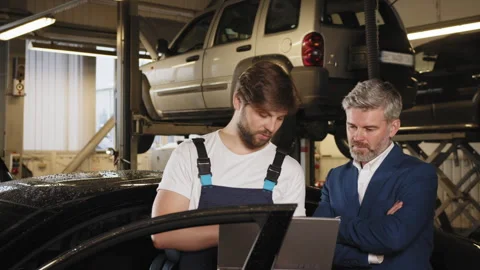 Auto mechanic showing data on the computer for mature haired male customer. Gray Stock Footage 243365422