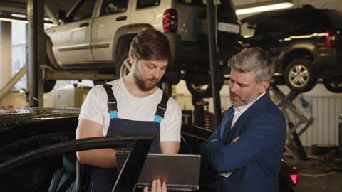 Auto mechanic showing data on the computer for mature haired male customer. Gray Stock Footage 243366250