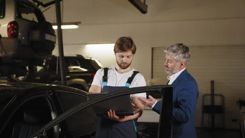 Auto mechanic showing data on the computer for mature haired male customer. Gray Stock Footage 243367138