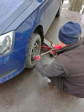 The auto mechanic sits down next to the wheel of the car and unscrews Stock Photos