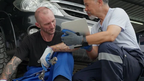 An auto mechanic sitting in front of a car talking to his supervisor Stock Footage 246134229