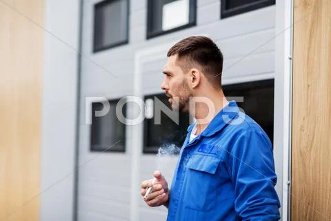 Auto mechanic smoking cigarette at car workshop Stock Photos