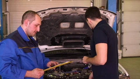 Auto mechanic tells the owner of the machine about the repairs done in garage Stock Footage 75685367
