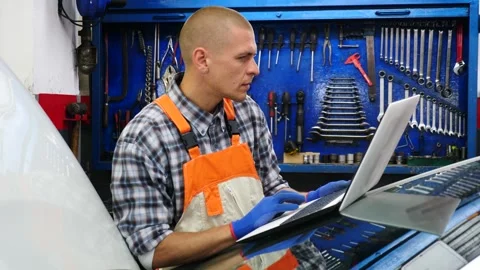 Auto mechanic in uniform doing engine diagnostics with computer in the car Stock Footage 254999754