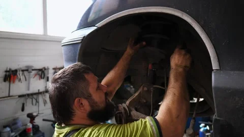 Auto mechanic in uniform works underneath a lifting vehicle at workshop Stock Footage 326042429