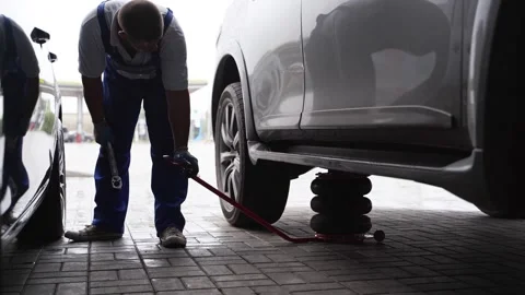 Auto mechanic uses hydraulic jack to lift car for tire change at garage. Man in Video stock 265154396
