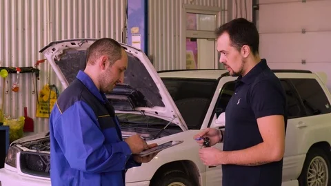 Auto Mechanic using a gadget while doing tests on a car in a garage with car Stock Footage 75683925