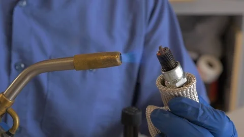 Auto mechanic using a torch to burn off carbon on spark plug. Video stock 100524307