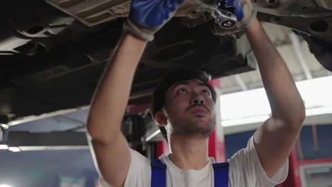 Auto mechanic using a wrench to tighten the nut on the car's suspension Stock Footage 208968012