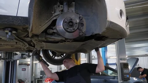 An auto mechanic working under the car on a car lift in the garage. Stock Footage 297844405