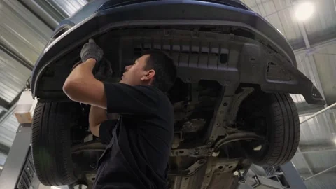 An auto mechanic working under the car on a car lift in the garage. Car service. Stock Footage 336666931