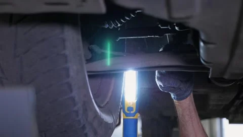 An auto mechanic working under a car on a car lift in a garage. Auto repair shop Stock Footage 337733886