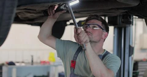 Auto mechanic working underneath car lifting machine at the garage. Car aut.. Stock Photos