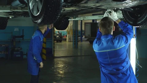 Auto mechanics working underneath a lifted car Stock Footage 70646703