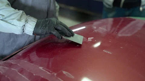 Auto paint man tears off damaged paint with a spatula from parts of a car hood Stock Footage 153487785