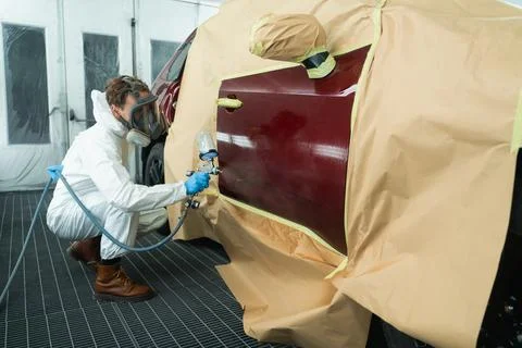 Auto painter in a protective suit and mask sprays a degreaser 스톡 사진