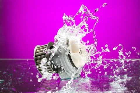 Auto parts, engine cooling pump in spurts of water on purple background Foto stock