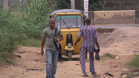 Auto rickshaw bumps down Nigerian road. Disabled man and another man walks past Stock Footage 86760917