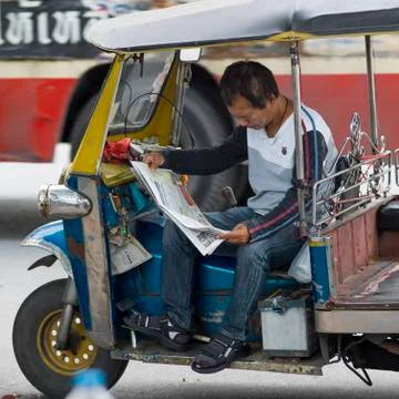 Auto rickshaw driver reading a newspaper at roadside, Bangkok, Thailand Stock Photos