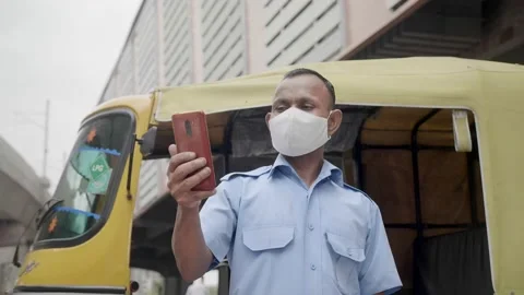 An auto-rickshaw driver wearing face mask and using mobile phone Stock Footage 136669040