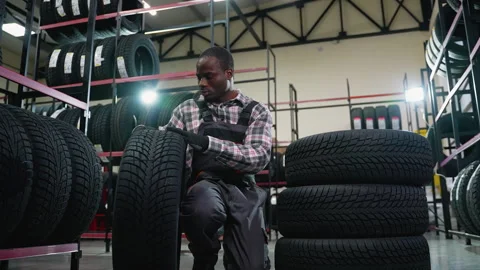Auto shop worker inspecting and stacking tires in warehouse Stock Footage 301559130