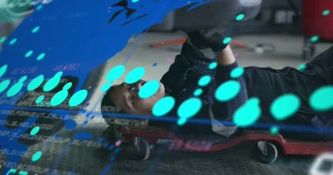 Auto tech lying on red creeper reaching under car on digital overlay appearing, 動画素材 333967803