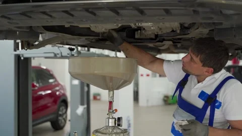 Auto technician changes oil under lifted car in garage. Mechanic drains old Stock Footage 271595452