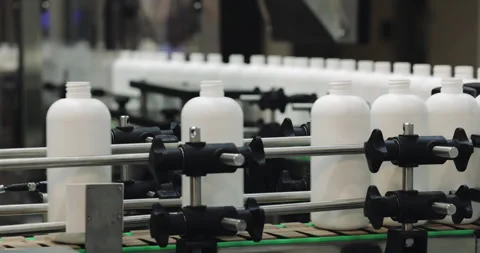 Automated machinery handles row of empty opaque plastic bottles in processing Stock Footage 346226527