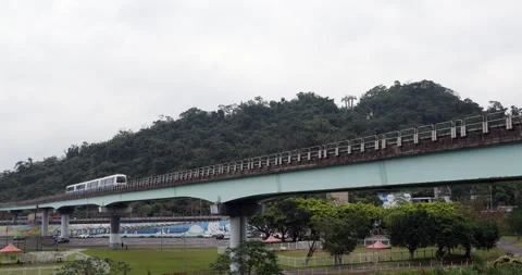 Automated metro train traveling on elevated viaduct against lush green hill Vídeo Stock 341100731