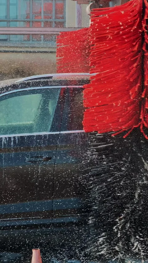 Automatic car wash machine cleaning side of black vehicle with red rotating Stock Footage 330782715