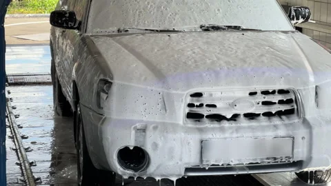 Automatic car wash. The SUV covered by active foam stands inside a carwash Stock Footage 200797832