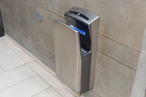 An automatic hand dryer is mounted on a bathroom wall, promoting hygiene an.. Stock Photos