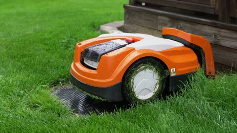 Automatic lawn robot mower under rain at charging stations on the grass Vídeos de archivo 205606796