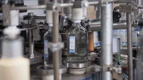 Automatic machine glues excise stamps on vodka bottles. Spill of vodka in glass Vídeos de archivo 127780847