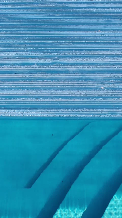 The automatic pool cover is halfway open, revealing clear blue water and built-i Stock Footage 312753877