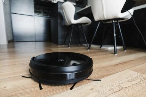 Automatic robot vacuum cleaner in black on wooden floor. New modern technolog Stock Photos