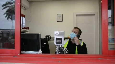 Automatic temperature measuring device and a security guard talking on the phone Stock Footage 147056970