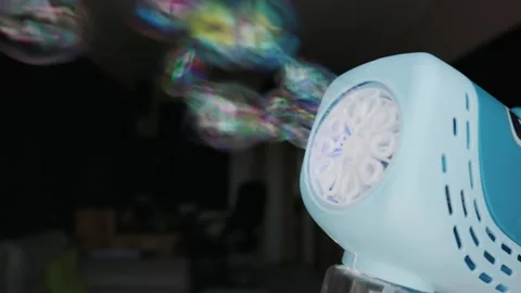 Automatic Toy Bubble Gun Blowing a Colorful Soap Bubble in Dark Room Stock Footage 339176686