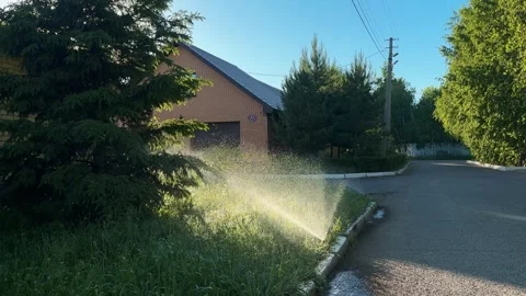 Automatic watering of the lawn in the yard with an irrigator. Spray flying on Stock Footage 346689926