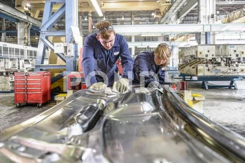 Automotive Apprentices Wearing Boiler Suits Working On Section Of Metal In Car