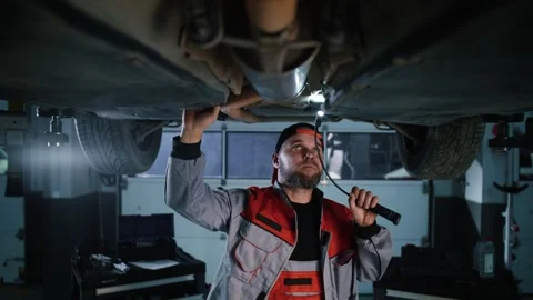 Automotive engineer holding a torch, is inspecting the underside of car Stock Footage 340580795
