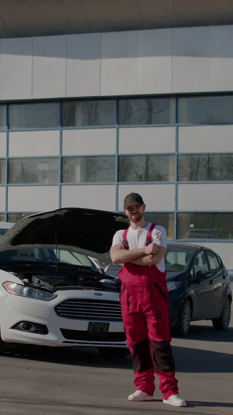 Automotive technician stands confidently next to vehicle holding wrench looks Stock Footage 275158053