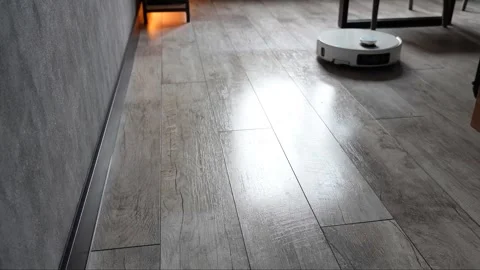 Autonomous robotic vacuum cleaner navigating across grey wooden flooring Stock Footage 345023956