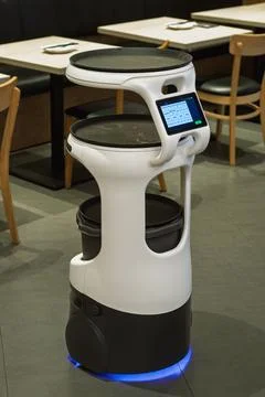 Autonomous service robot waits between restaurant tables, ready to deliver Stock Photos