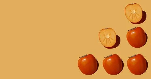 Autumn pattern is made with half a persimmon on a orange background. Stock Photos