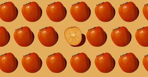 Autumn pattern is made with half a persimmon on a beige background. Stock Photos