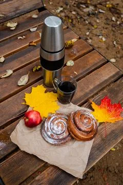 Autumn picnic setup with thermos, coffee mugs, cinnamon rolls, apple, and y.. Stock Photos